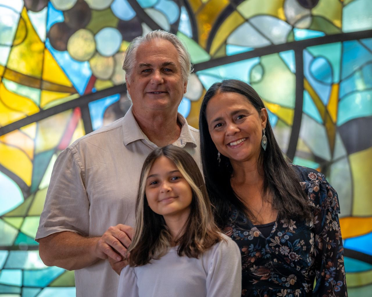 Pastor Craig with his wife Alessandra and daughter Alyssia in front of a stained glass window