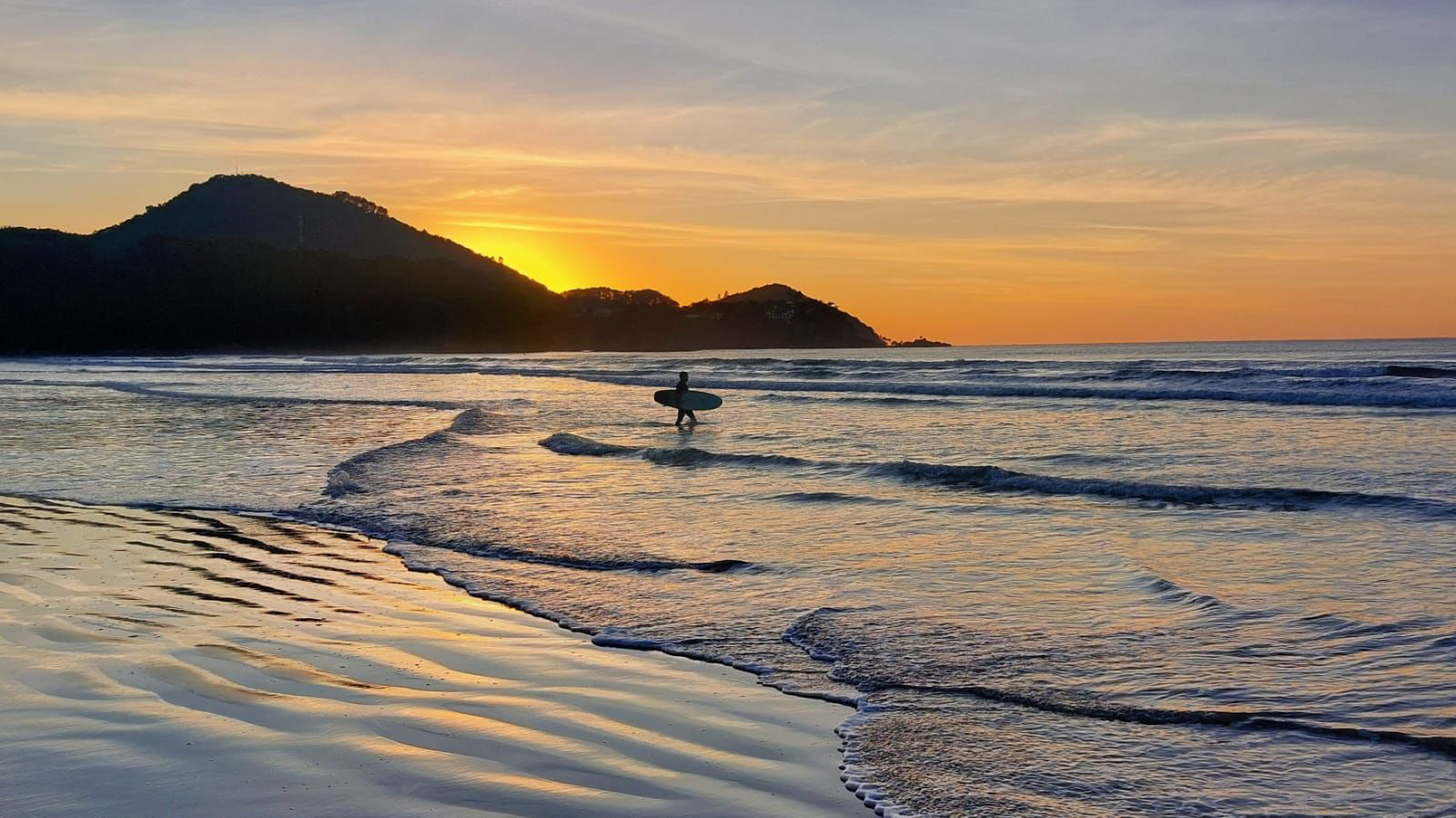 Surfer walking into the ocean at sunset on a Brazilian beach